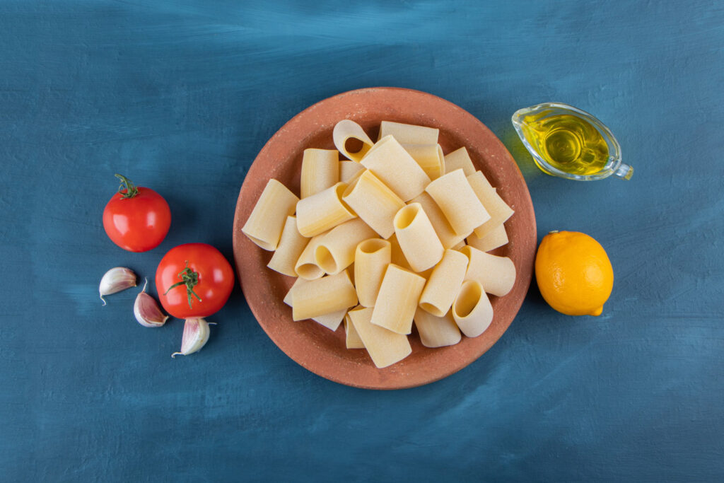 A brown plate of raw cannelloni pasta with fresh red tomatoes and lemon on a dark-blue background