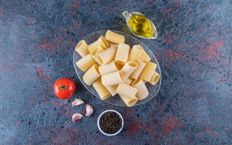 A glass plate of raw cannelloni pasta with garlic and oil on a dark surface